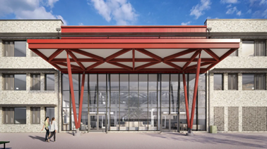 Front entrance of a modern school building with a wide glass façade. A large red steel canopy with triangular beams projects outward above the doors, supported by angled columns. Light‑coloured brick walls with rows of windows frame the entrance. Two people walk across an open paved area in front. The sky is blue with scattered clouds, and benches and bins sit near the entrance.